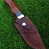 The Damascus steel knife snugly nestled in its handmade leather sheath.