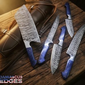 Hand-forged Damascus steel kitchen knife set, 9–14 inch blades, with blue honeycomb handles and leather roll bag on rustic bladesmith workbench.