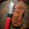 Custom Damascus Tanto knife with red wooden handle and hand-tooled leather sheath on a rustic American workbench