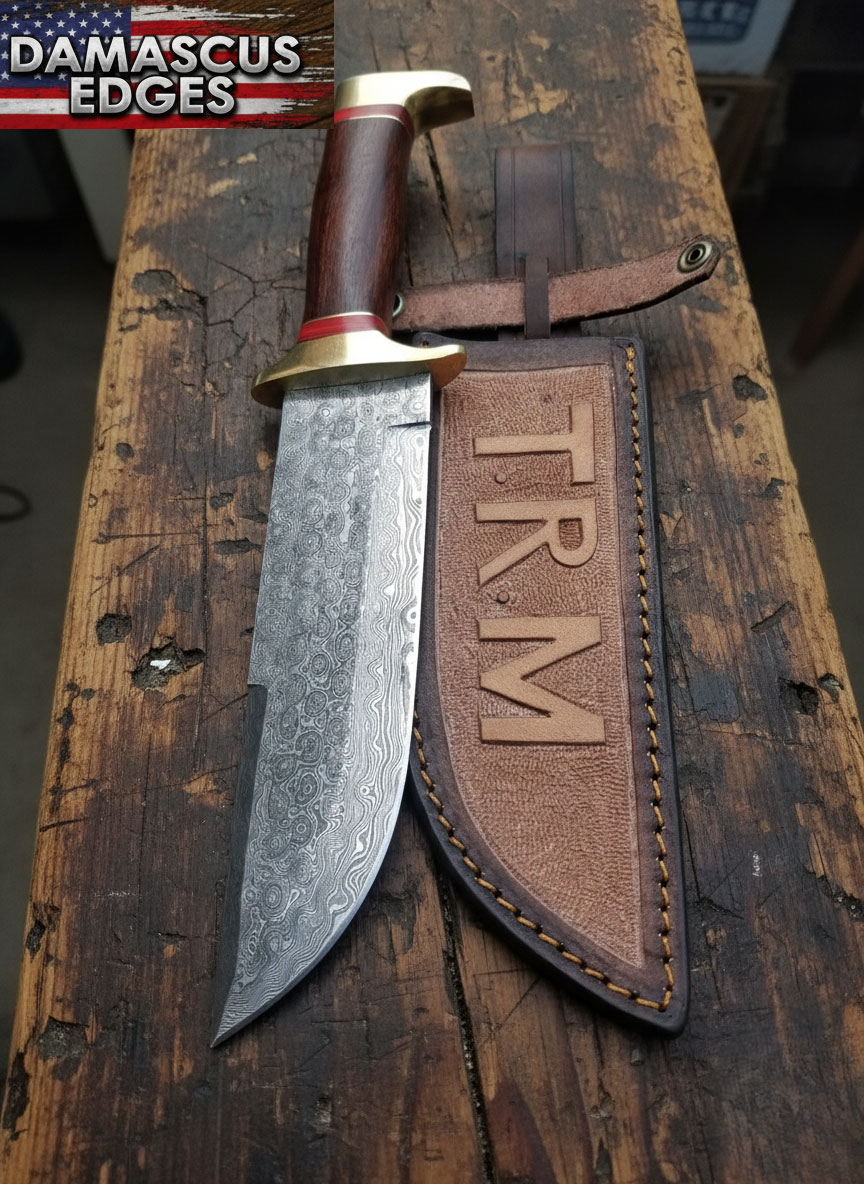 13-Inch Raindrop Damascus Bowie Knife with Custom Leather Sheath – Handmade by Damascus Edges Hand-forged 13-inch Raindrop Damascus Bowie knife with polished wooden handle and engraved leather sheath labeled TRM, crafted by Damascus Edges on a rustic American workbench.