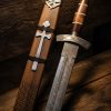 Hand-forged Damascus Viking sword with rosewood handle, bone spacer, and engraved wooden scabbard featuring a holy cross — crafted by Damascus Edges for American collectors.